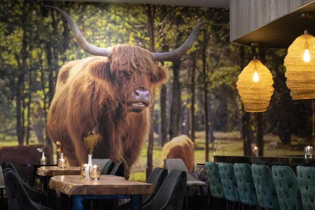 Ein Restaurantinnenraum mit einer großen Wandmalerei eines Jaks, Holztischen und hängenden Pendelleuchten.