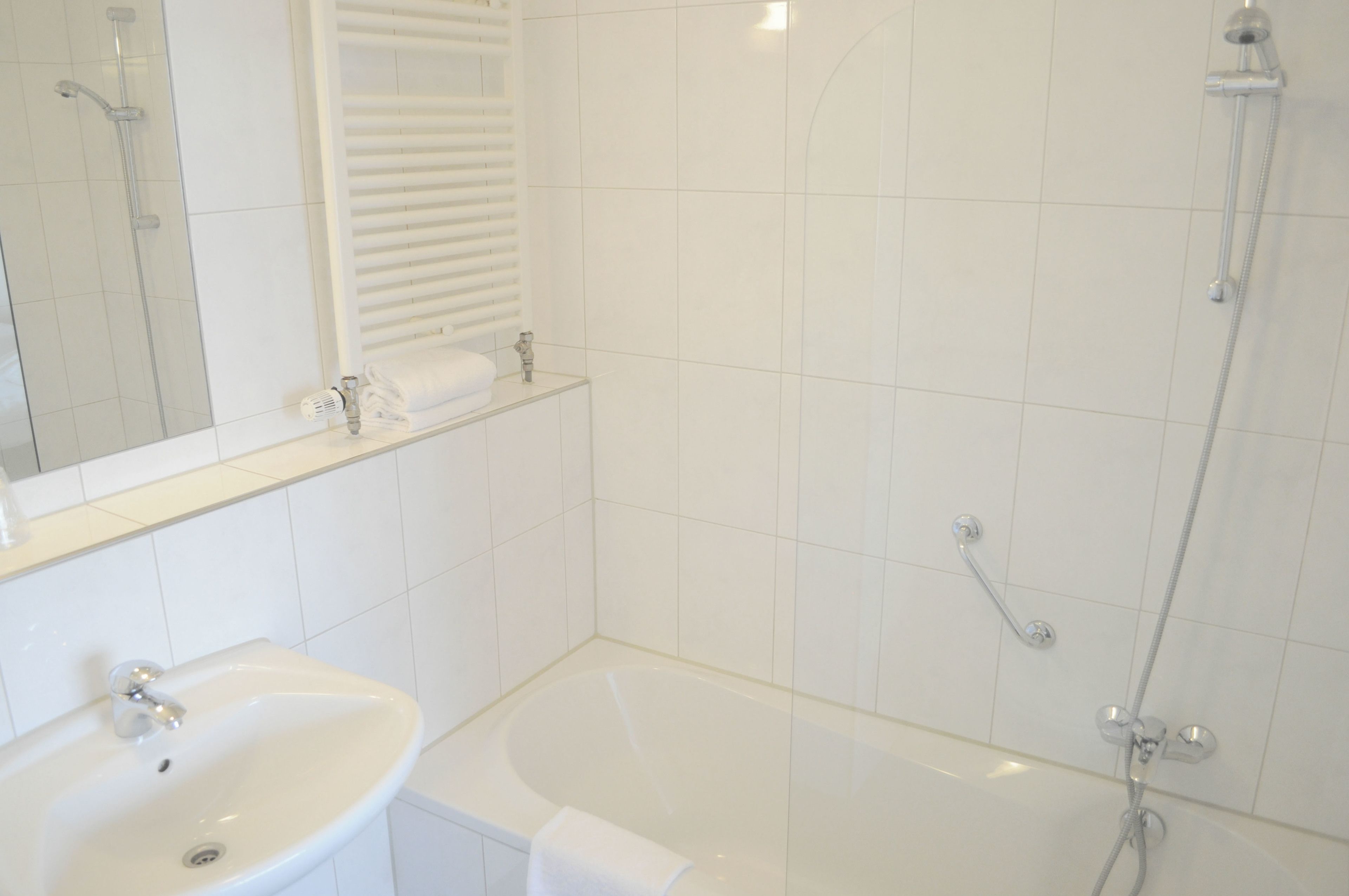 Un baño con lavabo, espejo, toallero y bañera con ducha.