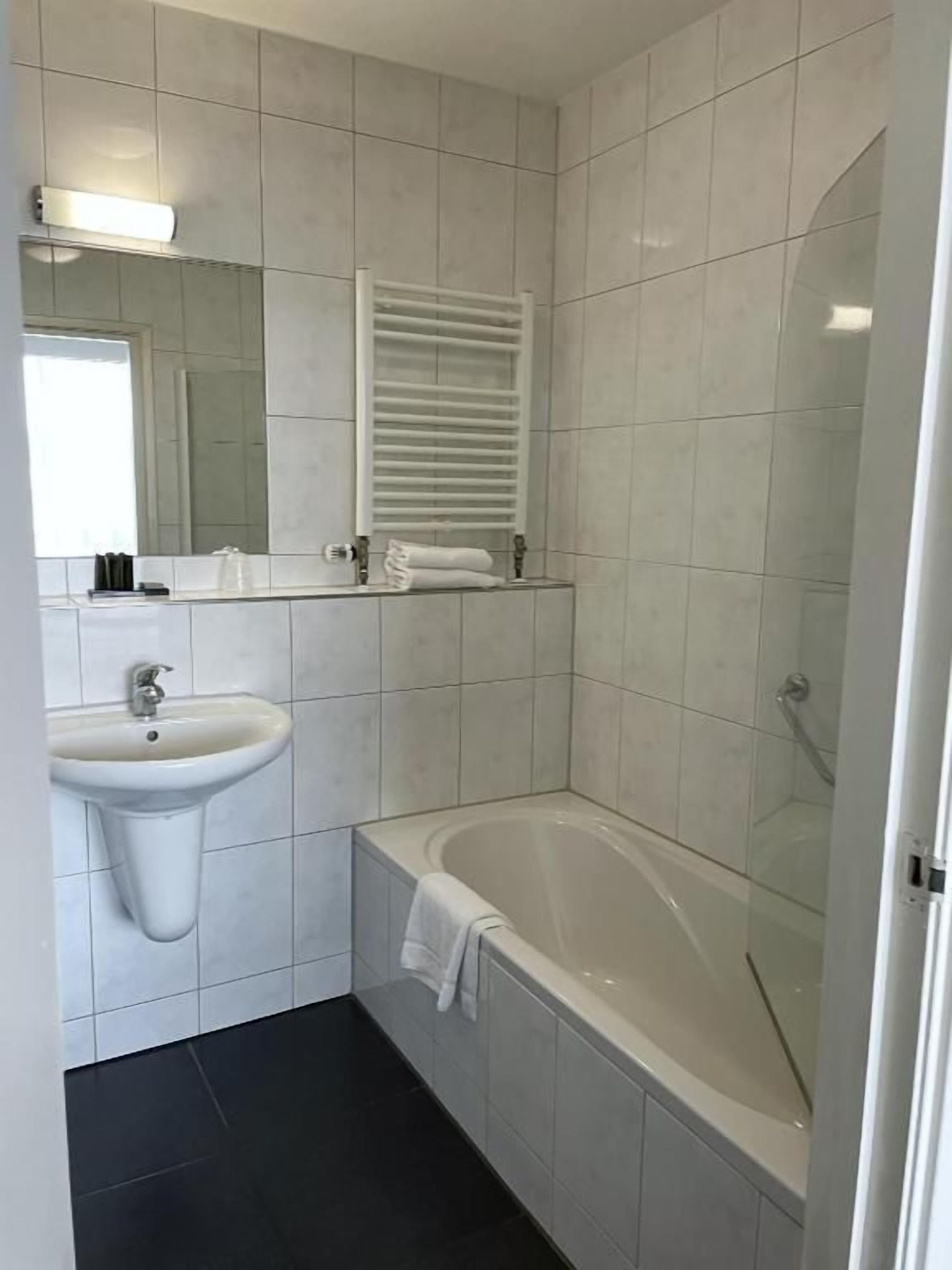 A bathroom with a sink, mirror, towel rack, and a bathtub.