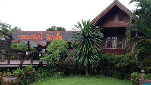 A traditional wooden building with a sign in a foreign script, surrounded by lush greenery and a well-maintained lawn. - Kannawat Resort (Ban Na)