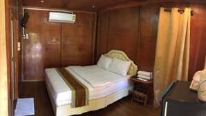 A small, cozy room with a single bed, a bedside table with a lamp, a small stool, and a heater on the wall. - Kannawat Resort (Ban Na)