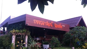 A building with a sign in a foreign language, surrounded by greenery and potted plants. - Kannawat Resort (Ban Na)