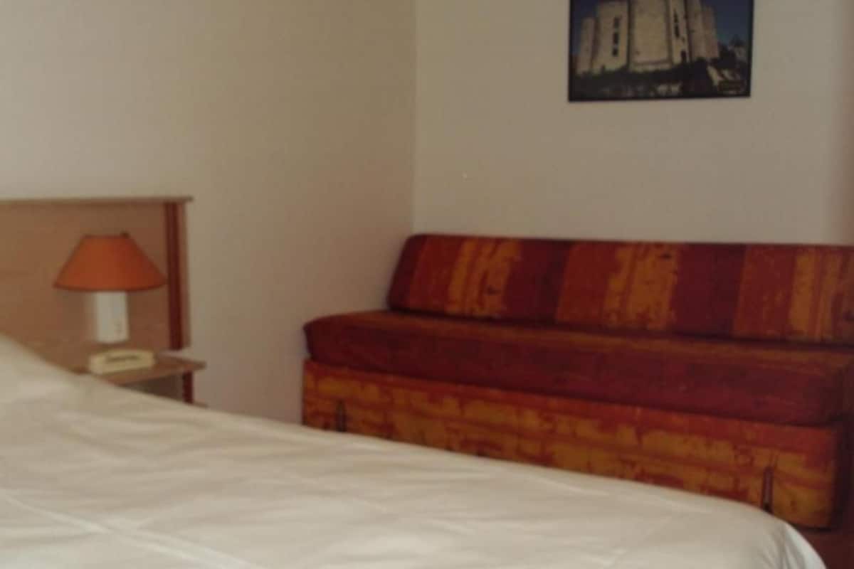 A hotel room with a bed, a nightstand with a lamp, and a wooden bench.