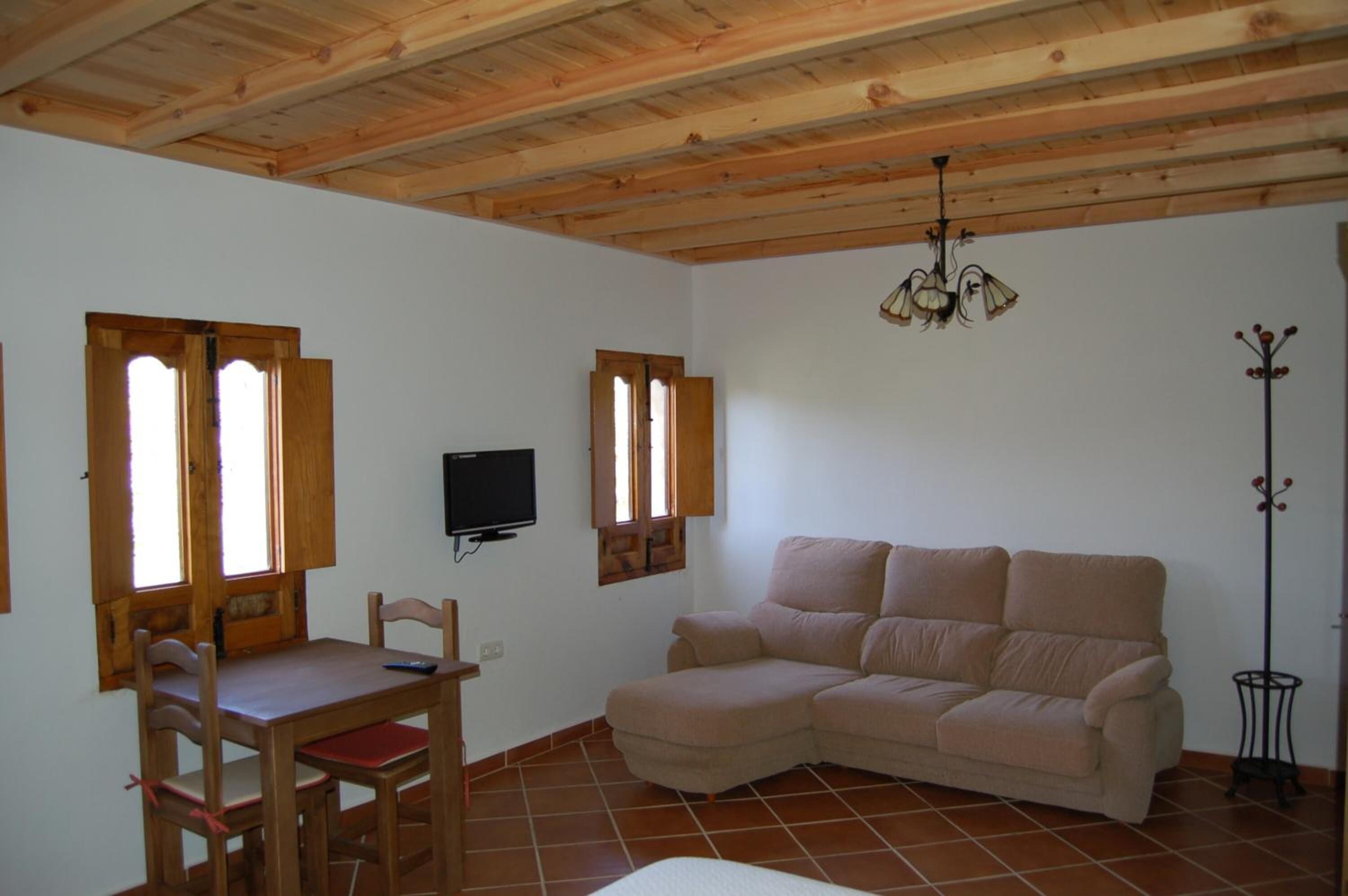 Una stanza con soffitto in legno, un divano beige, un tavolo da pranzo con sedie e un televisore a parete.