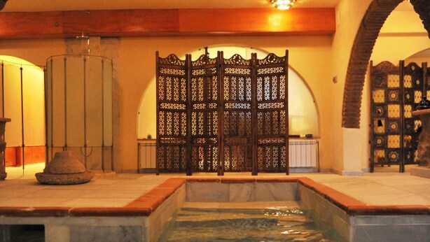 A pool area with a stone archway, a decorative wooden gate, and a tiled floor. - La Molinilla Apartamentos Y Hammam - Adults Only (Linares de la Sierra)