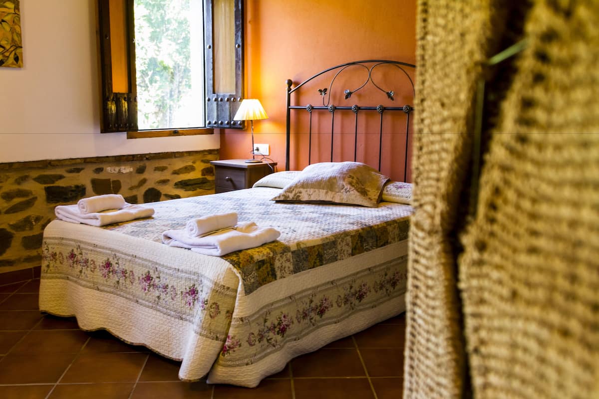 Ein Bett mit floralem Überwurf und Kissen, ein Nachttisch mit Lampe und eine Steinwand.