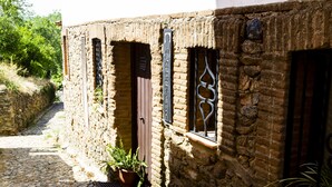 A narrow cobblestone street with a stone building featuring wooden shutters and a potted plant. - La Molinilla Apartamentos Y Hammam - Adults Only (Linares de la Sierra)