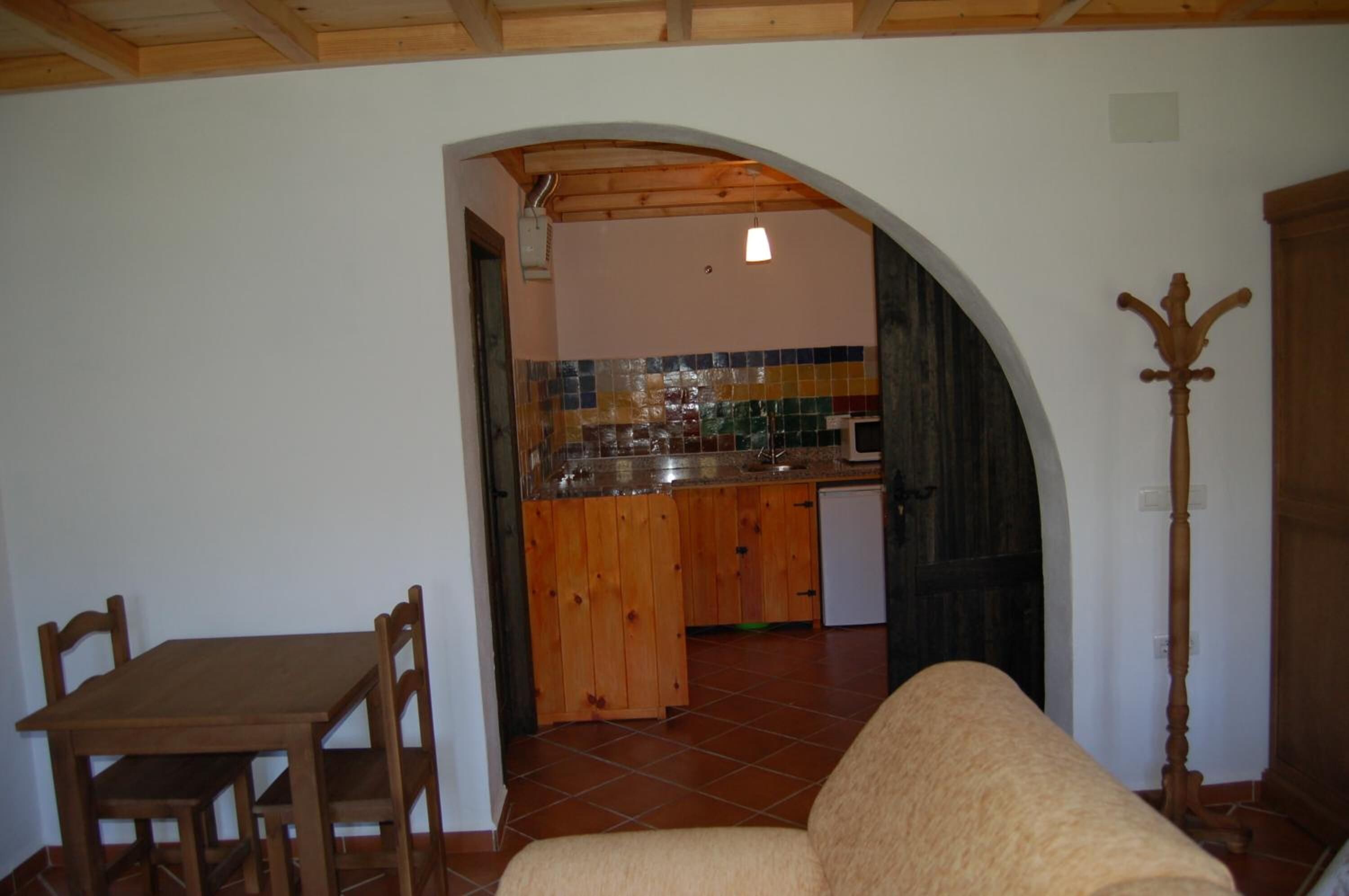 Una sala de estar acogedora con una mesa y sillas de madera, un sofá y una cocina con salpicadero de azulejos y armarios de madera.