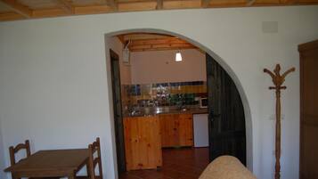 Una sala de estar acogedora con una mesa y sillas de madera, un sofá y una cocina con salpicadero de azulejos y armarios de madera.
