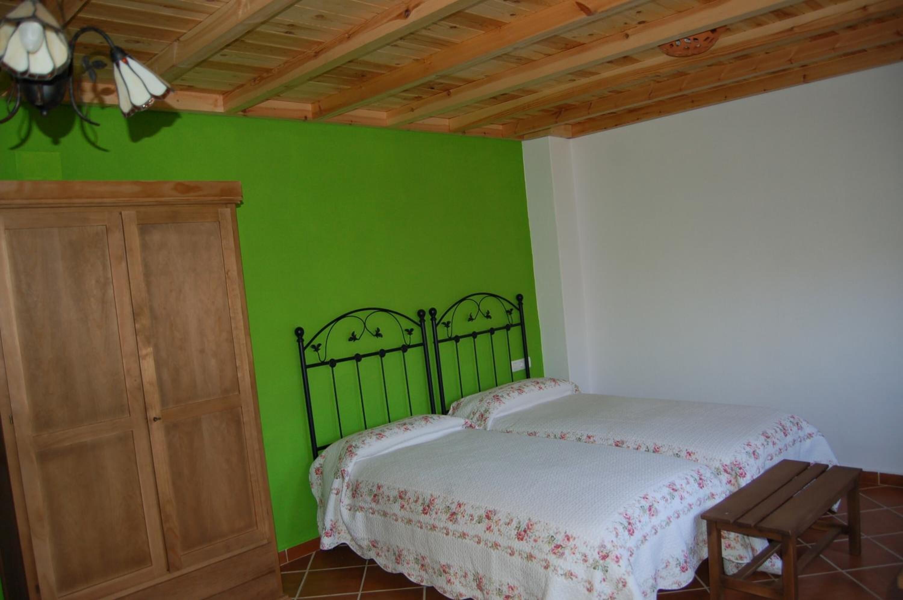Une pièce avec un lit en bois, une armoire en bois et un mur vert.