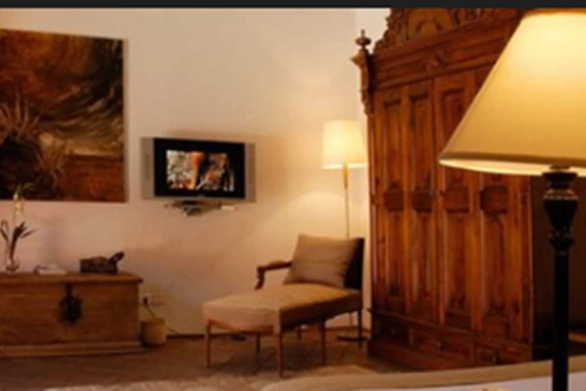 Een kamer met een houten kast, twee stoelen, een lamp en een schilderij aan de muur.