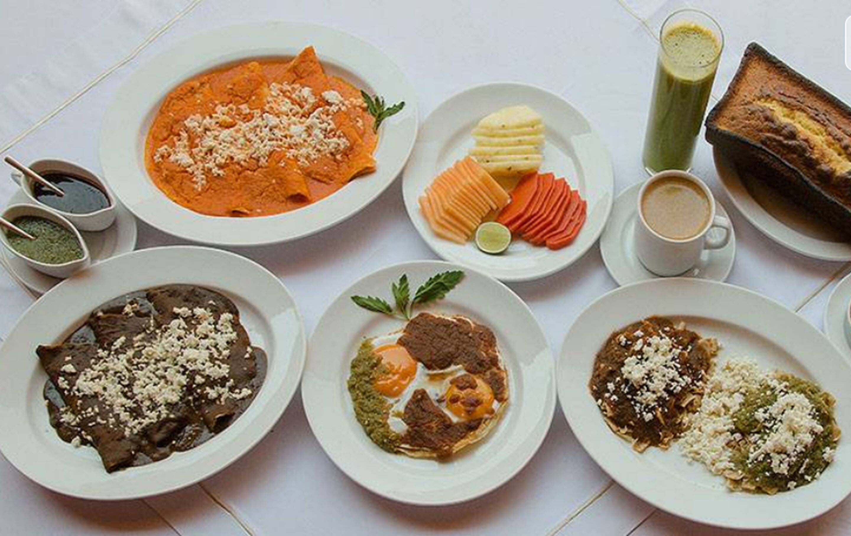 Una mesa con diversos platos, incluyendo enchiladas, un batido verde y un plato al horno.