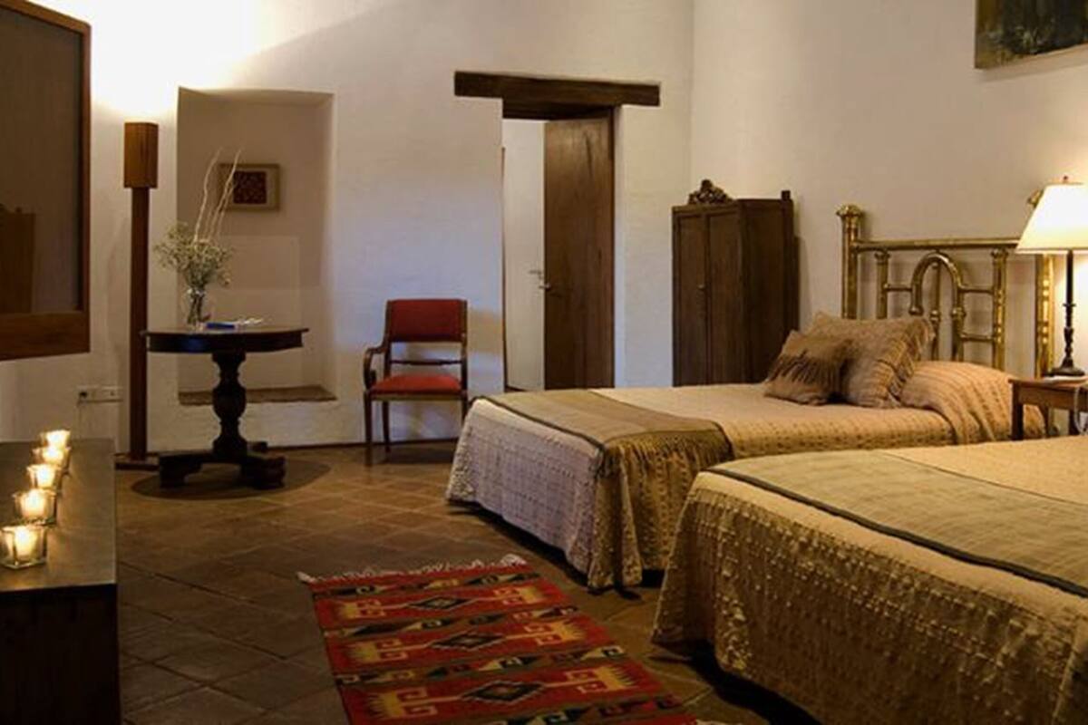 Een slaapkamer met twee bedden, een stoel, een tafel met kaarsen en een lamp.