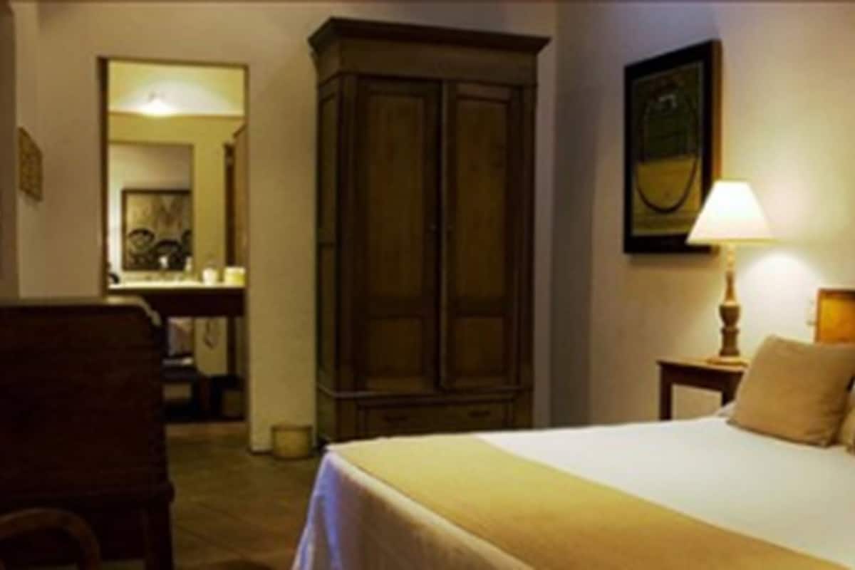 Een hotelkamer met een bed, een houten garderobe, een bureau met een lamp en een spiegel.