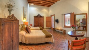 A bedroom with two beds, a wooden wardrobe, a bench, a table with candles, and a mirror.