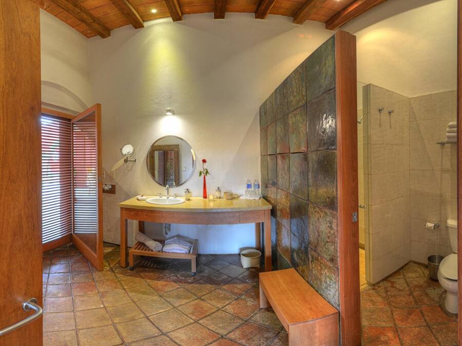 Un baño con tocador de madera, espejo redondo, banco y zona de ducha.