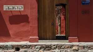 A red building with a wooden door, a stone wall, and a sign reading "TES OROS 805".