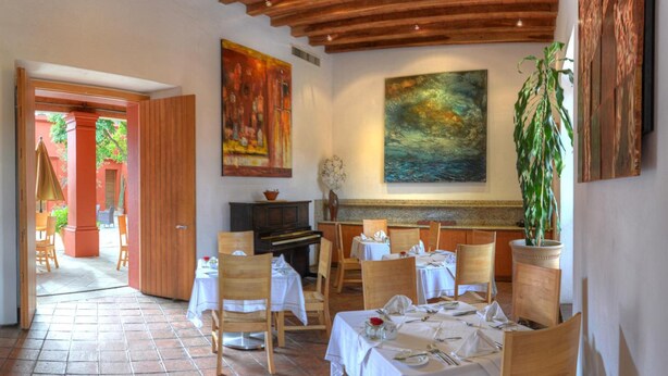 A dining area with wooden tables and chairs, a piano, and artwork on the walls.