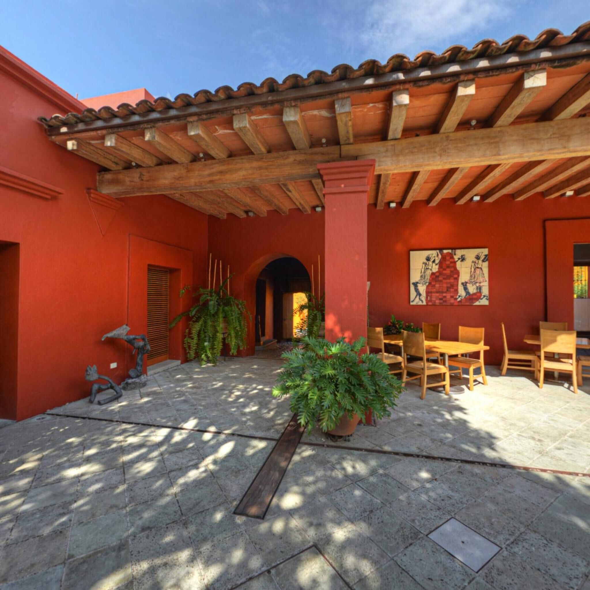 A courtyard with a tiled floor, wooden furniture, and potted plants.