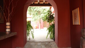 An arched doorway leading to a courtyard with potted plants and a framed picture on the wall.