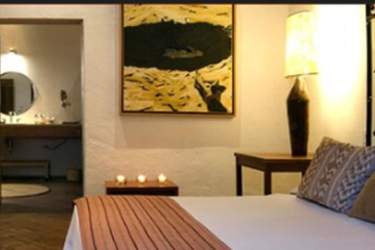 Een slaapkamer met een bed, nachtkastje, lamp en een schilderij aan de muur.