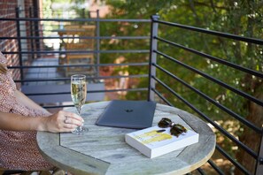 Une personne assise à une table ronde, devant un ordinateur portable, avec un verre de champagne et un livre.