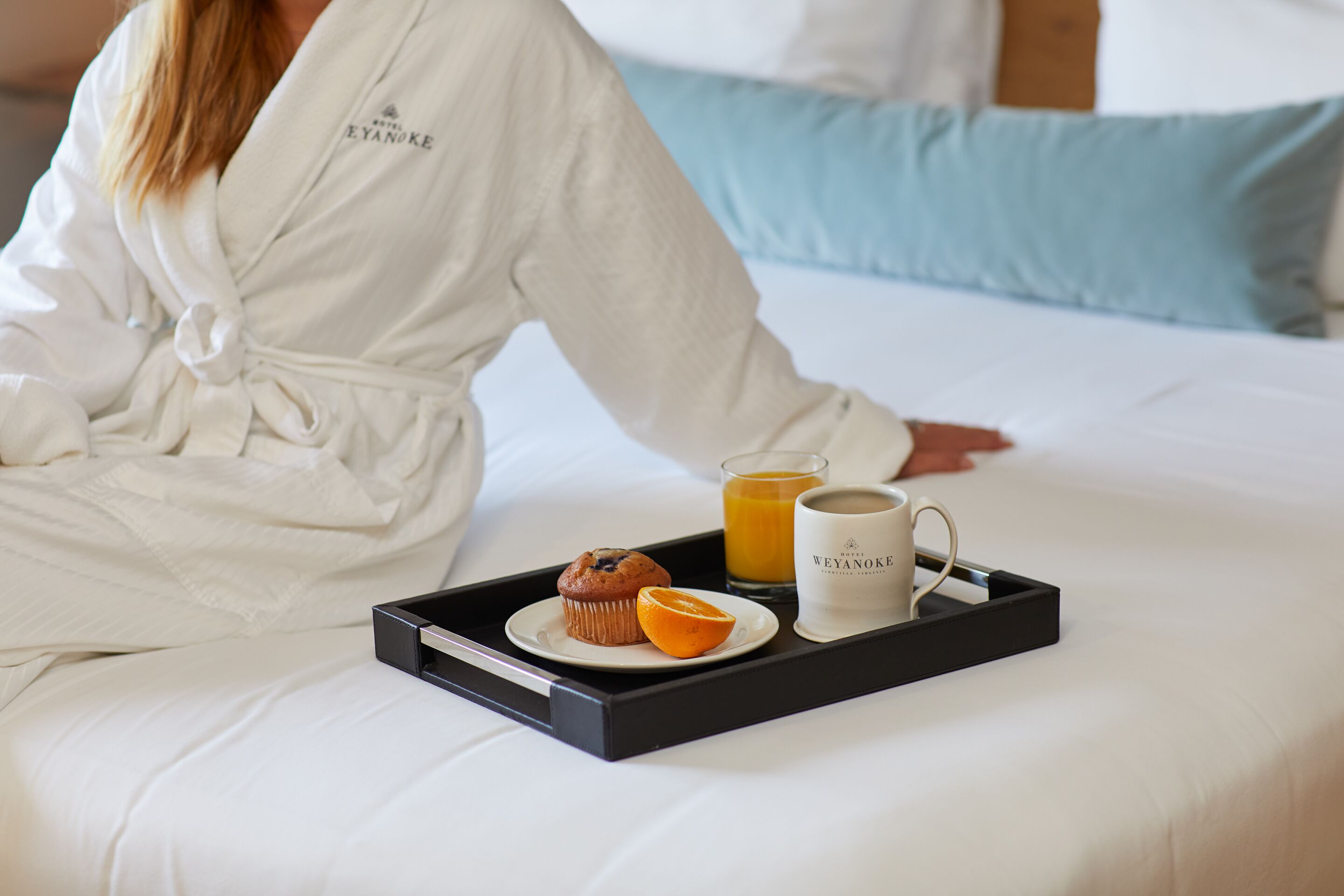A hotel room with a bed, a tray with a muffin, orange slice, and a mug.