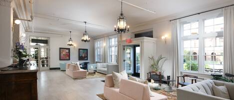 A spacious hotel lobby with a reception desk, seating areas, and large windows offering views of the outdoors.