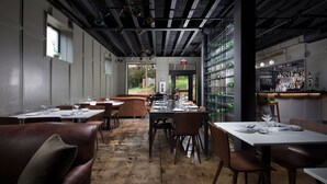 Een restaurant met een rustieke inrichting, met blootgelegde bakstenen muren, houten tafels en een bar voorzien van flessenplanken.