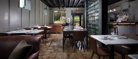 Ein Restaurant mit rustikalem Ambiente, das freiliegende Backsteinwände, Holztische und eine Theke mit Flaschenregalen zeigt.