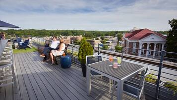 A rooftop deck with outdoor seating, a table with drinks, and a view of the cityscape.