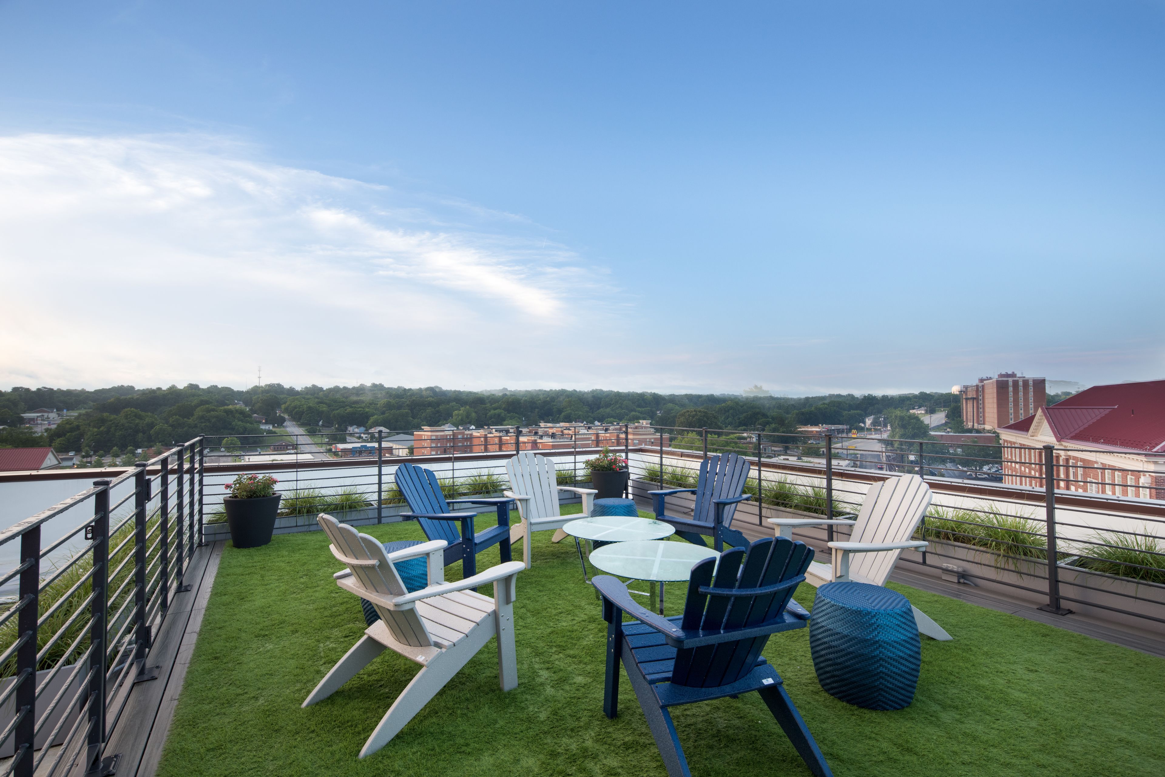 A rooftop terrace with green artificial grass, several Adirondack chairs, and a glass table.