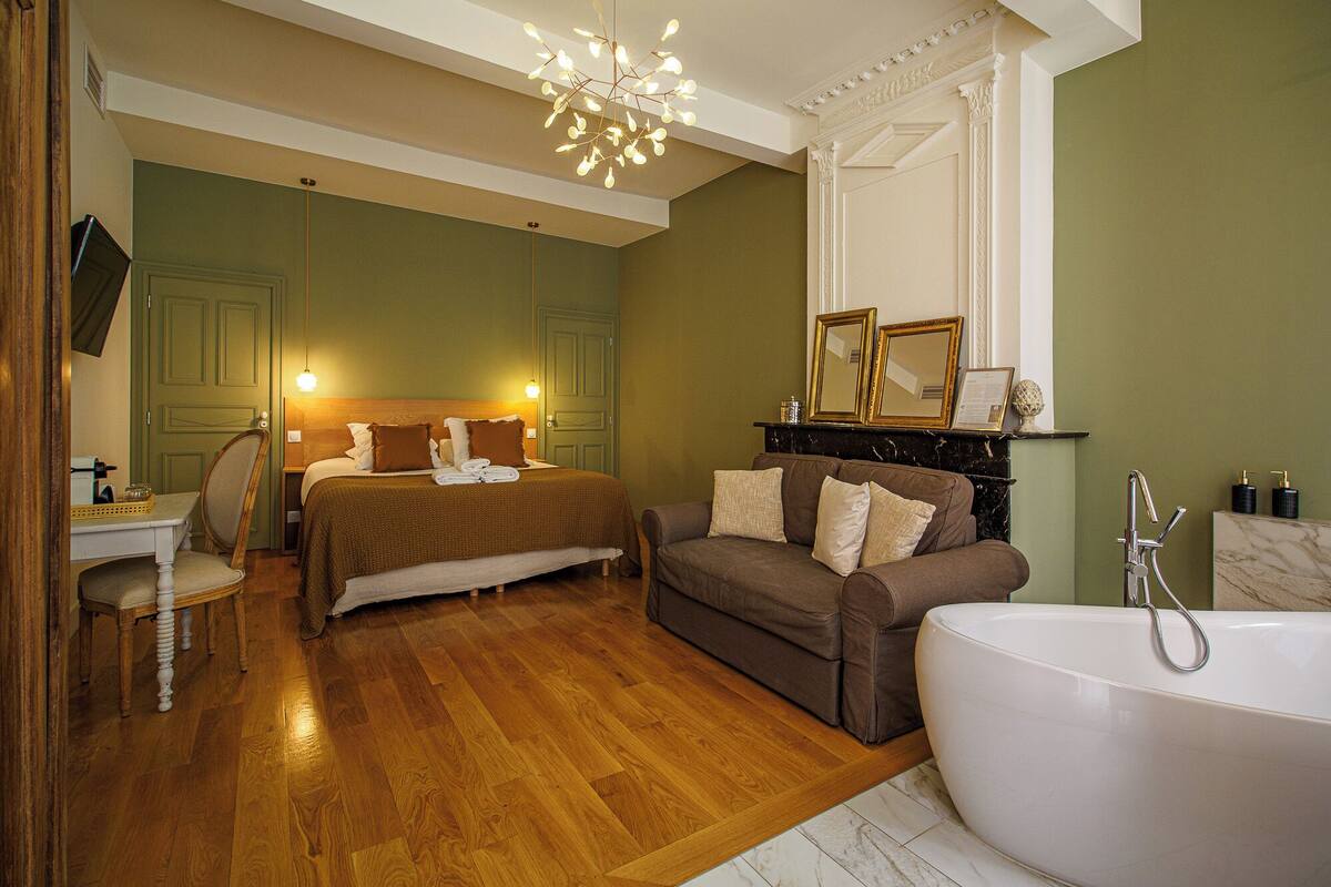 Une chambre à coucher élégamment aménagée, dotée d’un grand lit, d’un canapé et d’une baignoire sur pieds.