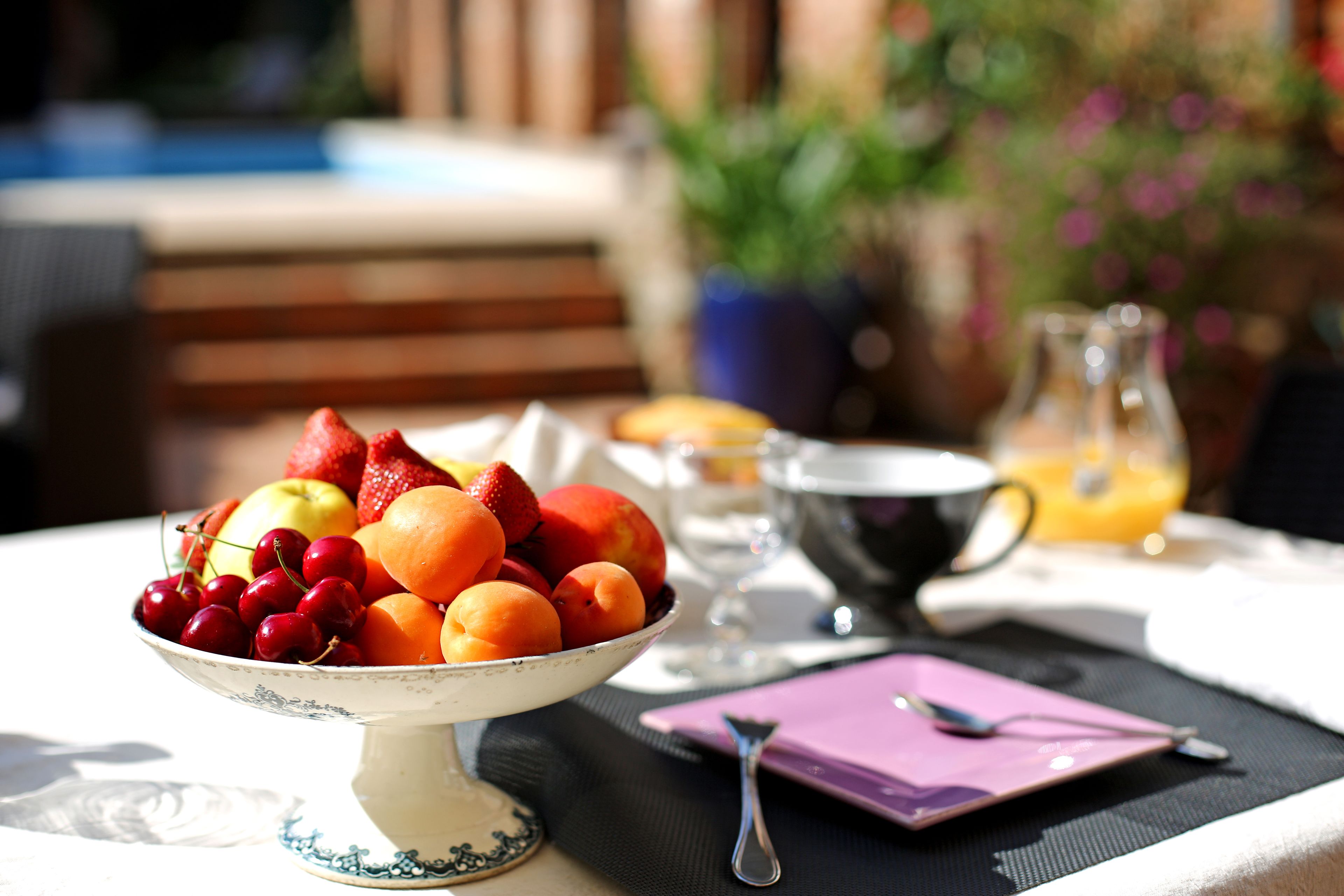 Una mesa con fruteros, una taza y un vaso de jugo de naranja.
