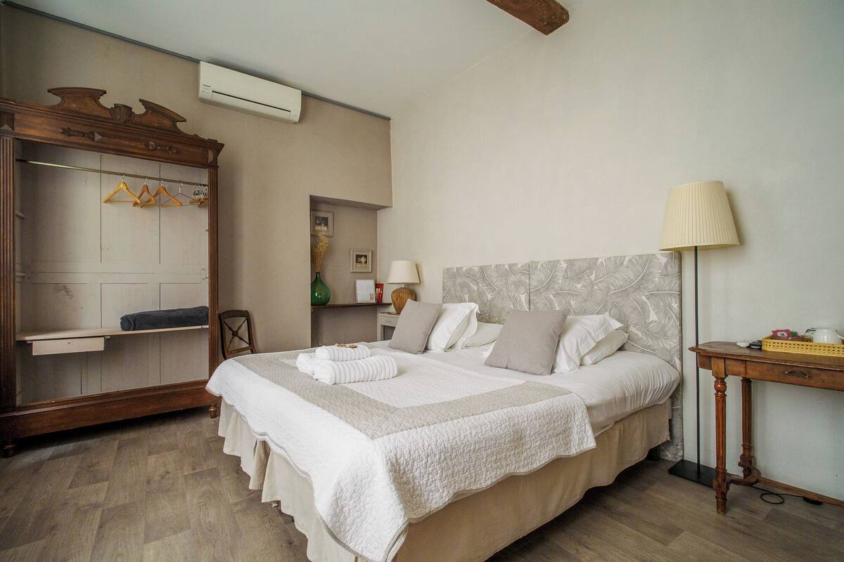 Un lit bien fait, avec une couette et des oreillers blancs, une armoire en bois, une table de chevet avec une lampe et un climatiseur fixé au mur.