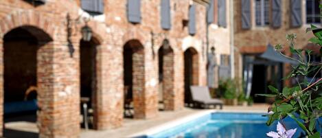 A poolside view of a building with brick arches and shuttered windows.
