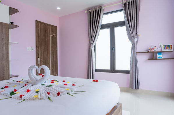 Una habitación de hotel con una cama bien hecha, una puerta de madera, una ventana con cortinas y un pequeño estante con objetos.