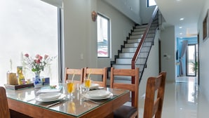 A dining area with a glass table, wooden chairs, and a staircase in the background. - Facetime Home (Da Nang)