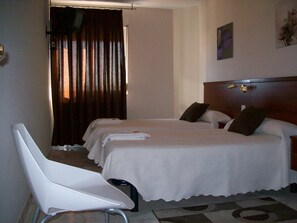 A hotel room with two beds, a white chair, and a wooden headboard.