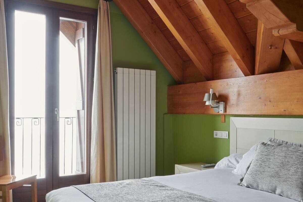 A bedroom with a bed, a nightstand, a window with curtains, and a radiator.