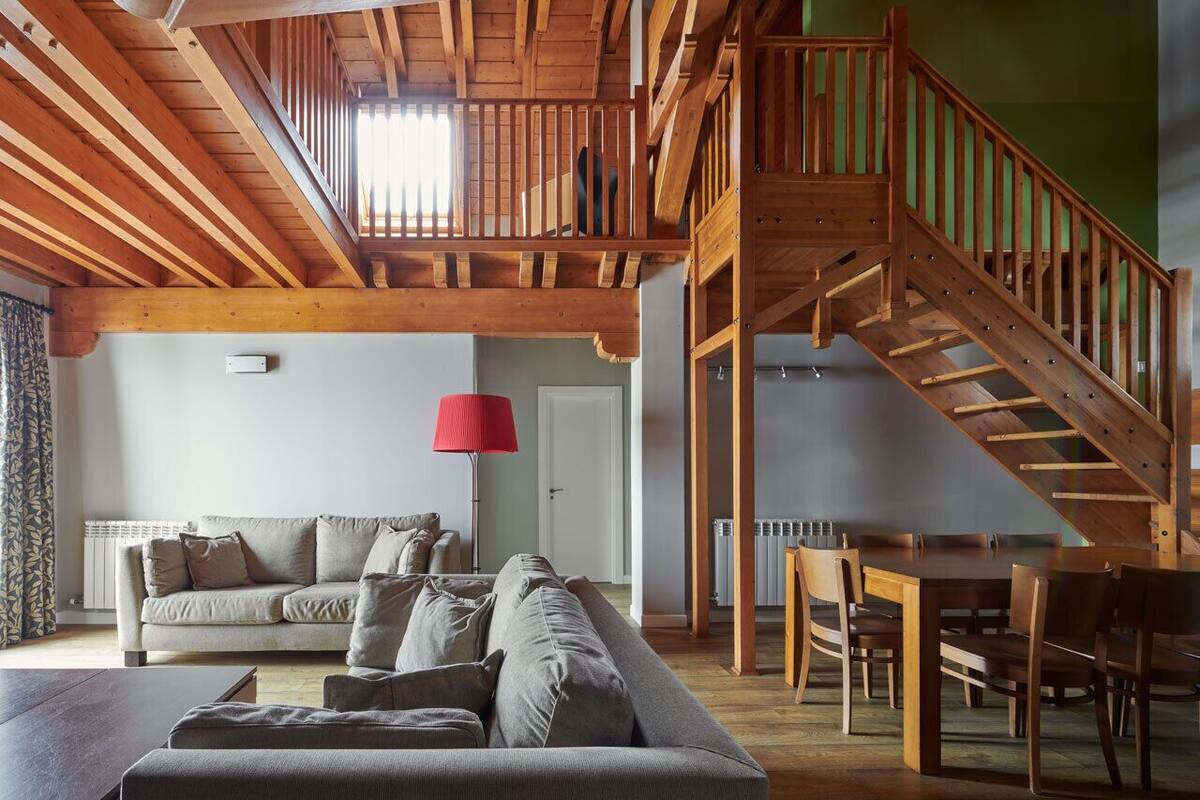 A spacious living room with a high ceiling, wooden staircase, and a dining area.