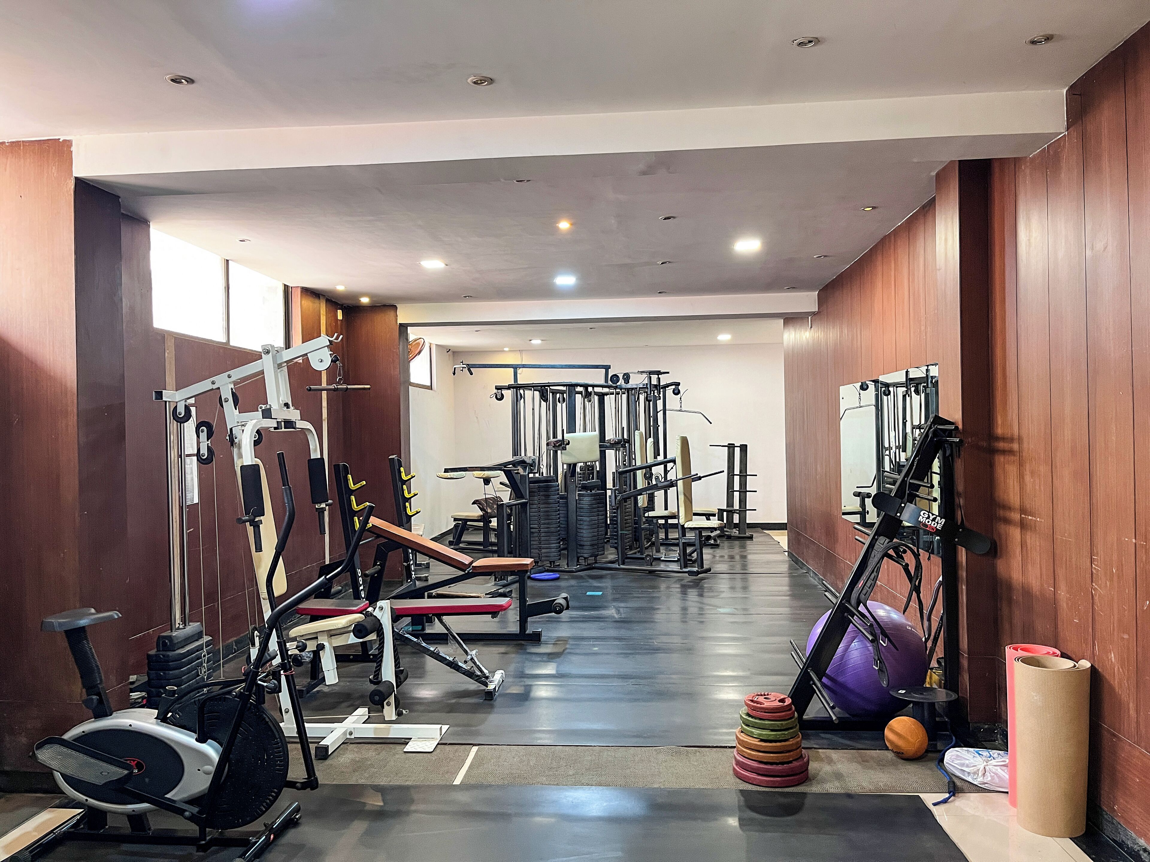 Ein Fitnessstudio mit verschiedenen Trainingsgeräten, darunter ein Laufband, Kraftgeräte und ein an der Wand befestigtes Fahrrad.