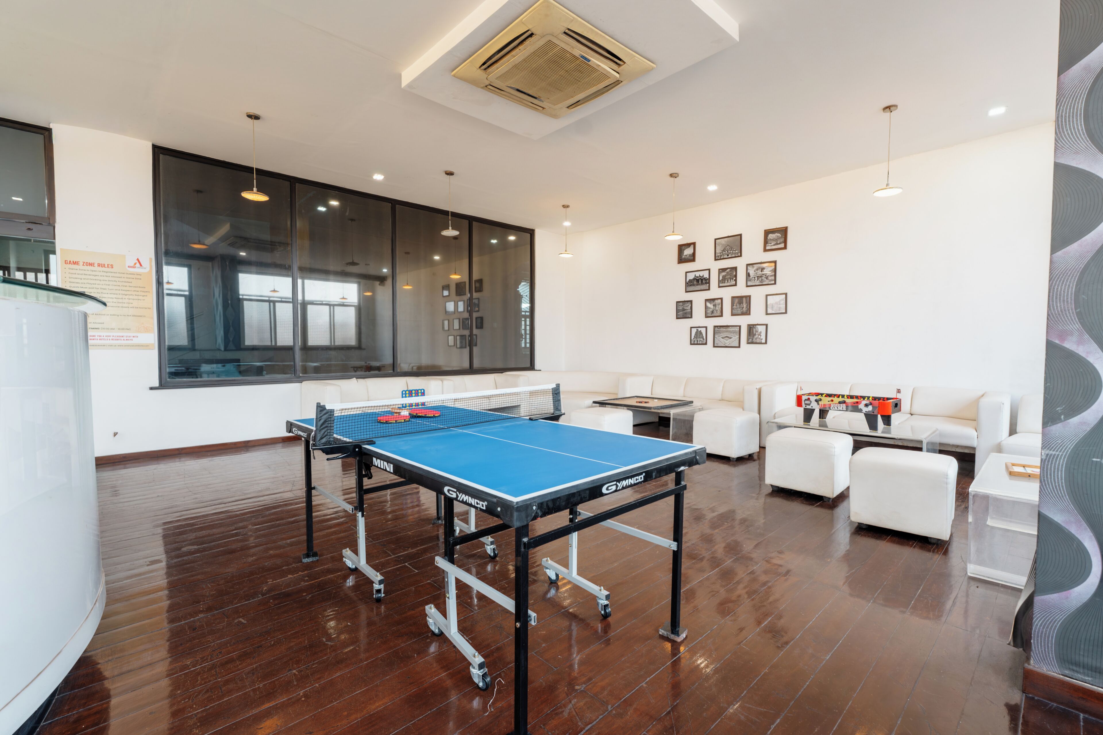 A spacious room with a ping pong table, white sofas, and a large window.