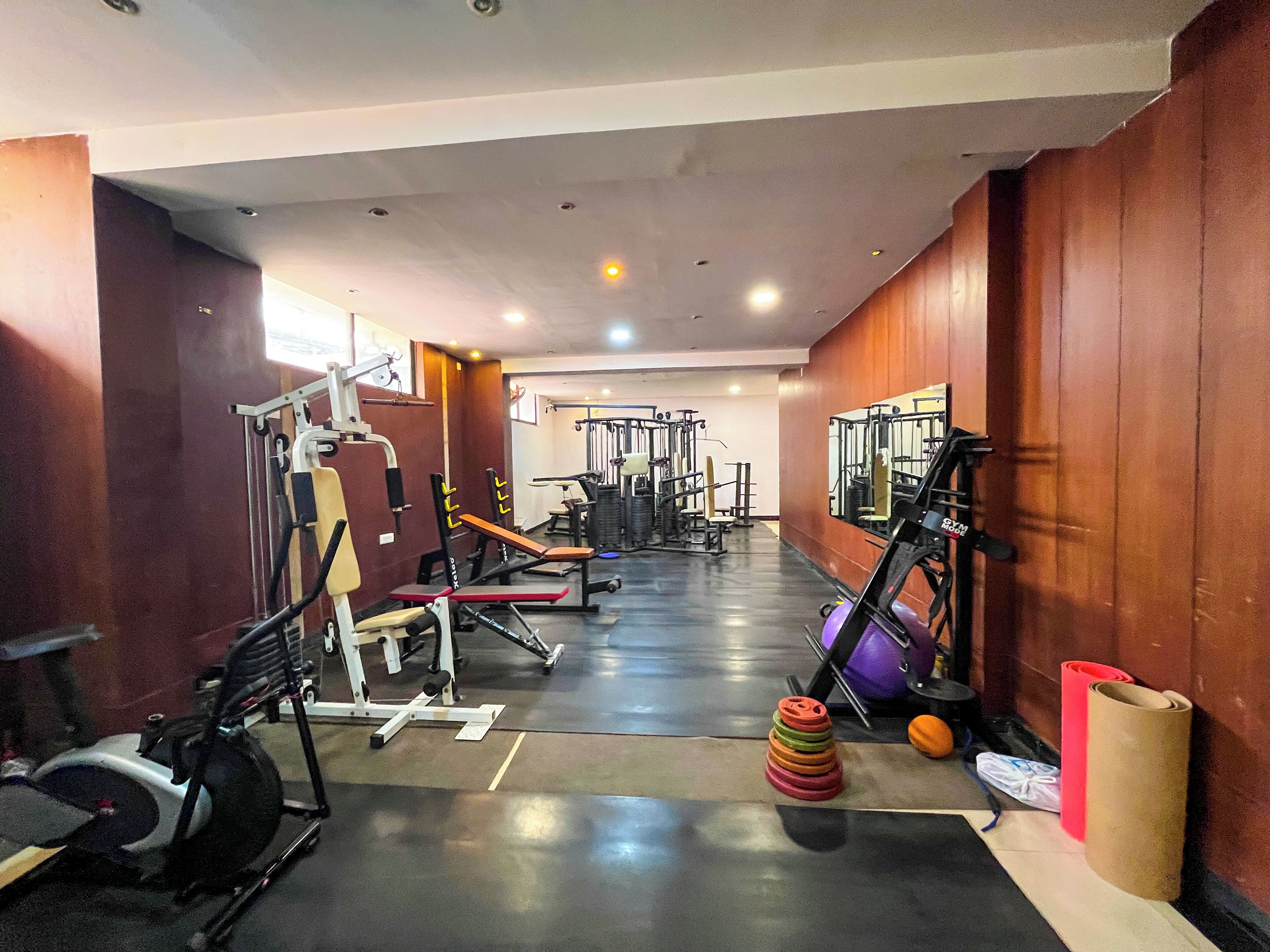 A gym with various exercise equipment, a mirror, and a stack of colorful dumbbells.