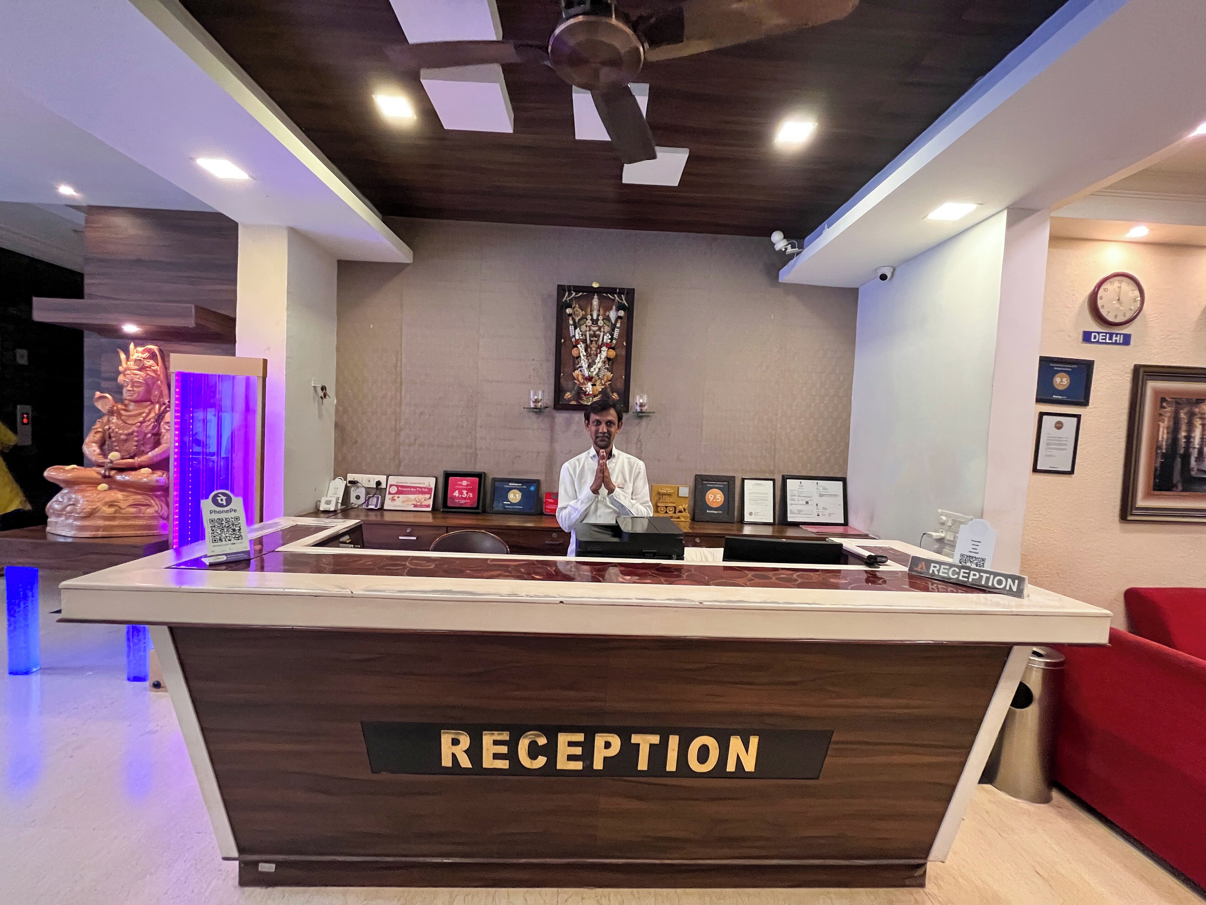 A reception desk labeled "RECEPTION" with framed certificates, a statue, and a clock on the wall.
