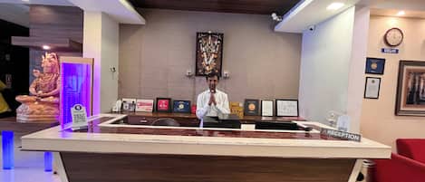 A reception desk labeled "RECEPTION" with framed certificates, a statue, and a clock on the wall.