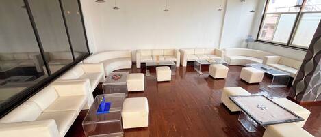 A modern living room with white leather sofas, clear glass coffee tables, and wooden flooring.