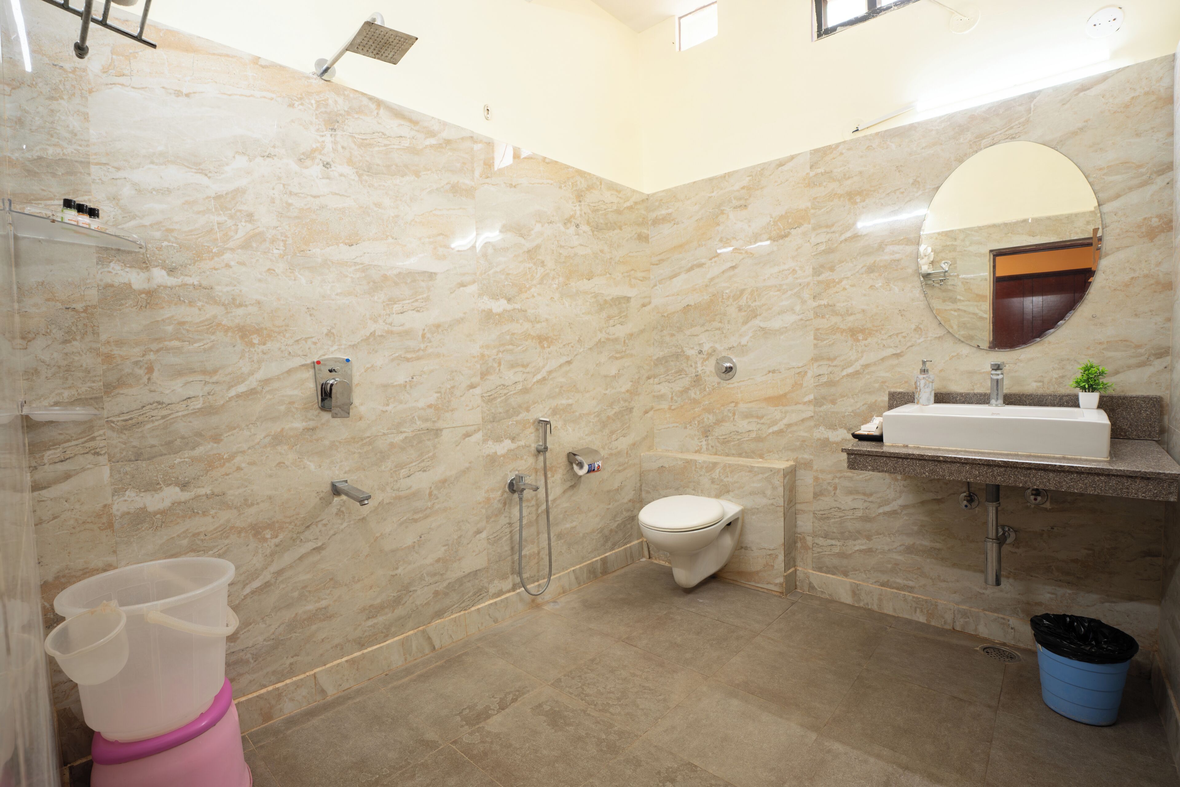 A bathroom with a marble wall, a toilet, a sink, a shower, and a mirror.