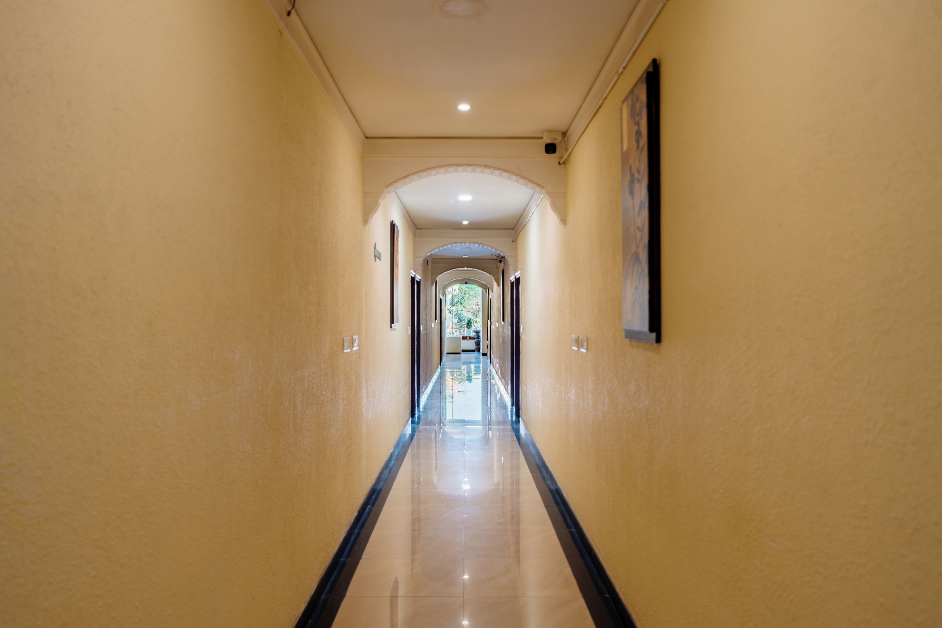 Un largo pasillo estrecho con piso pulido, arcos en las puertas y un cuadro enmarcado en la pared.