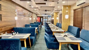 Un restaurant avec des banquettes et des tables recouvertes d’un tissu bleu, des éléments décoratifs en bois et des ventilateurs de plafond.